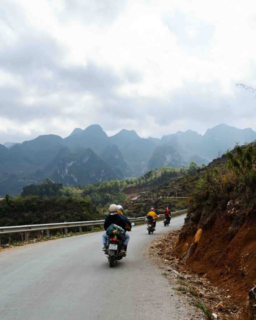 Group of travellers riding motorbikes along a winding mountain road on the Ha Giang Loop, Vietnam, with dramatic karst peaks in the background