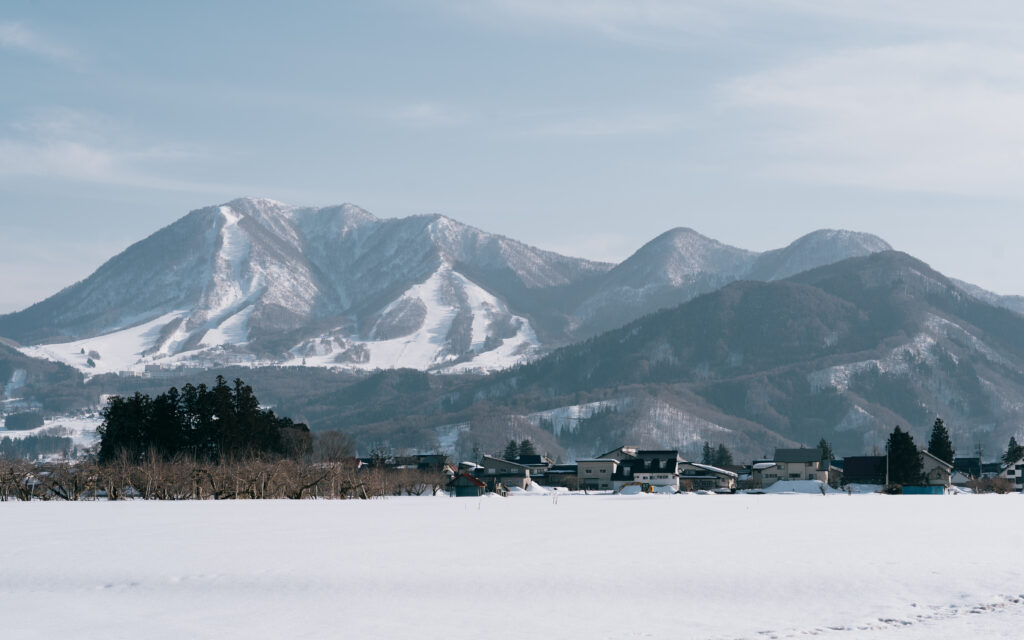 Wide view of Nozawa Onsen ski resort and surrounding snow-covered mountains in Japan, with a traditional village in the foreground
