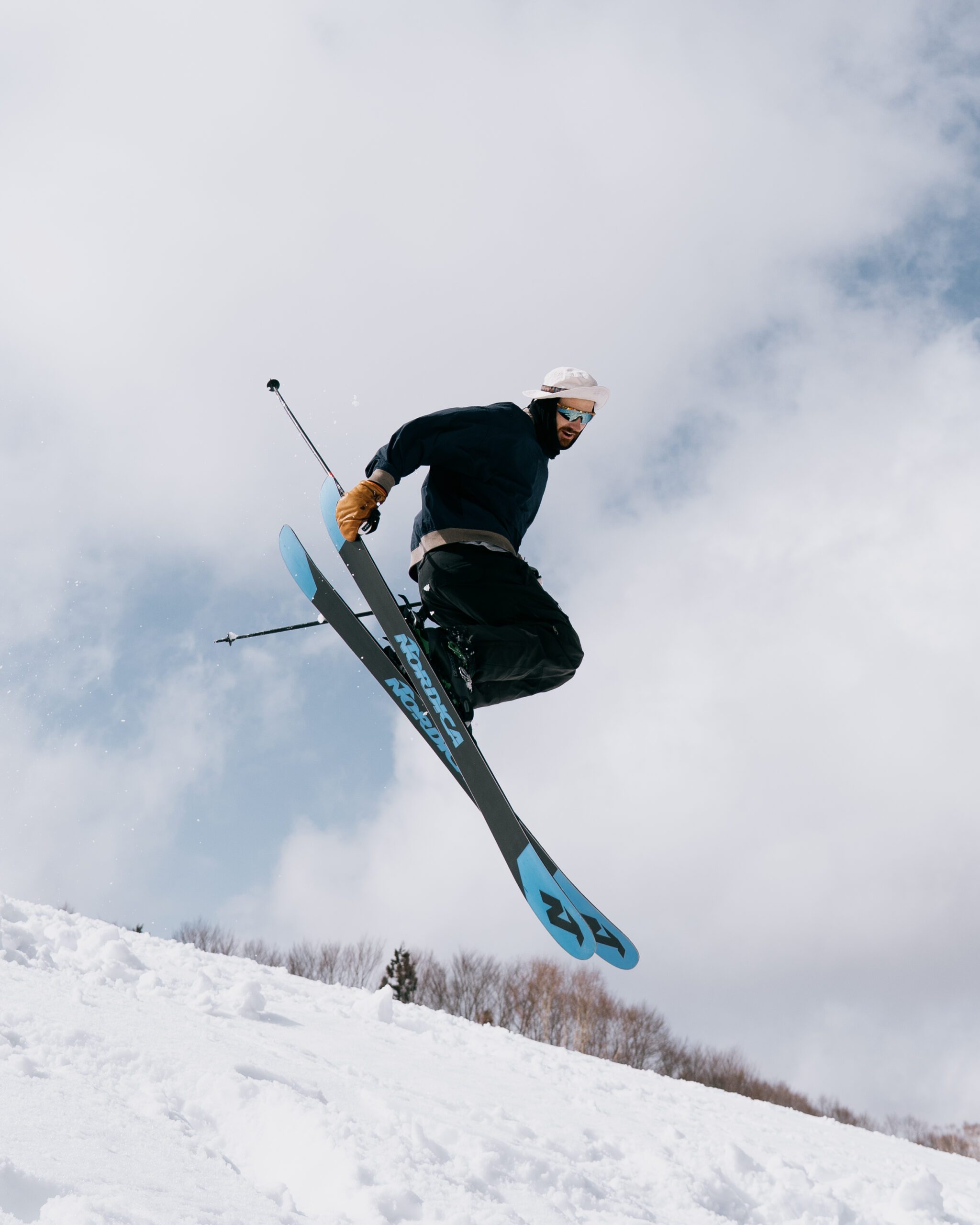 Skier catching big air off a jump on the slopes of Nozawa Onsen, Japan, wearing Nordica skis against a cloudy sky. Whilst working a ski season in Japan on a WHV