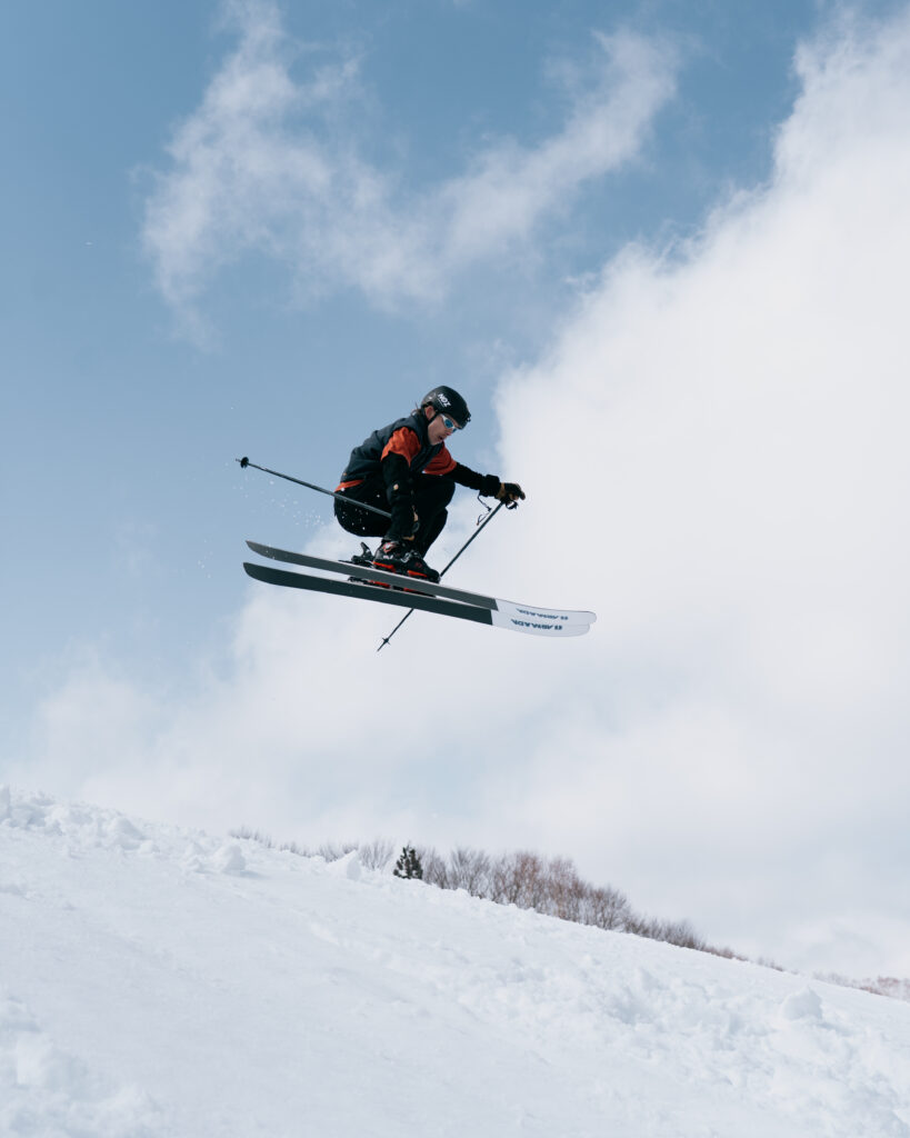 Skier launching off a homemade jump on the slopes of Nozawa Onsen, Japan, with snowy mountains in the background