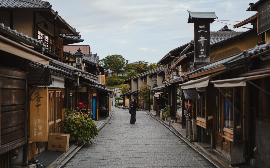Woman standing alone on a quiet historic street in Higashiyama, Kyoto, lined with traditional Japanese wooden shops and lanterns