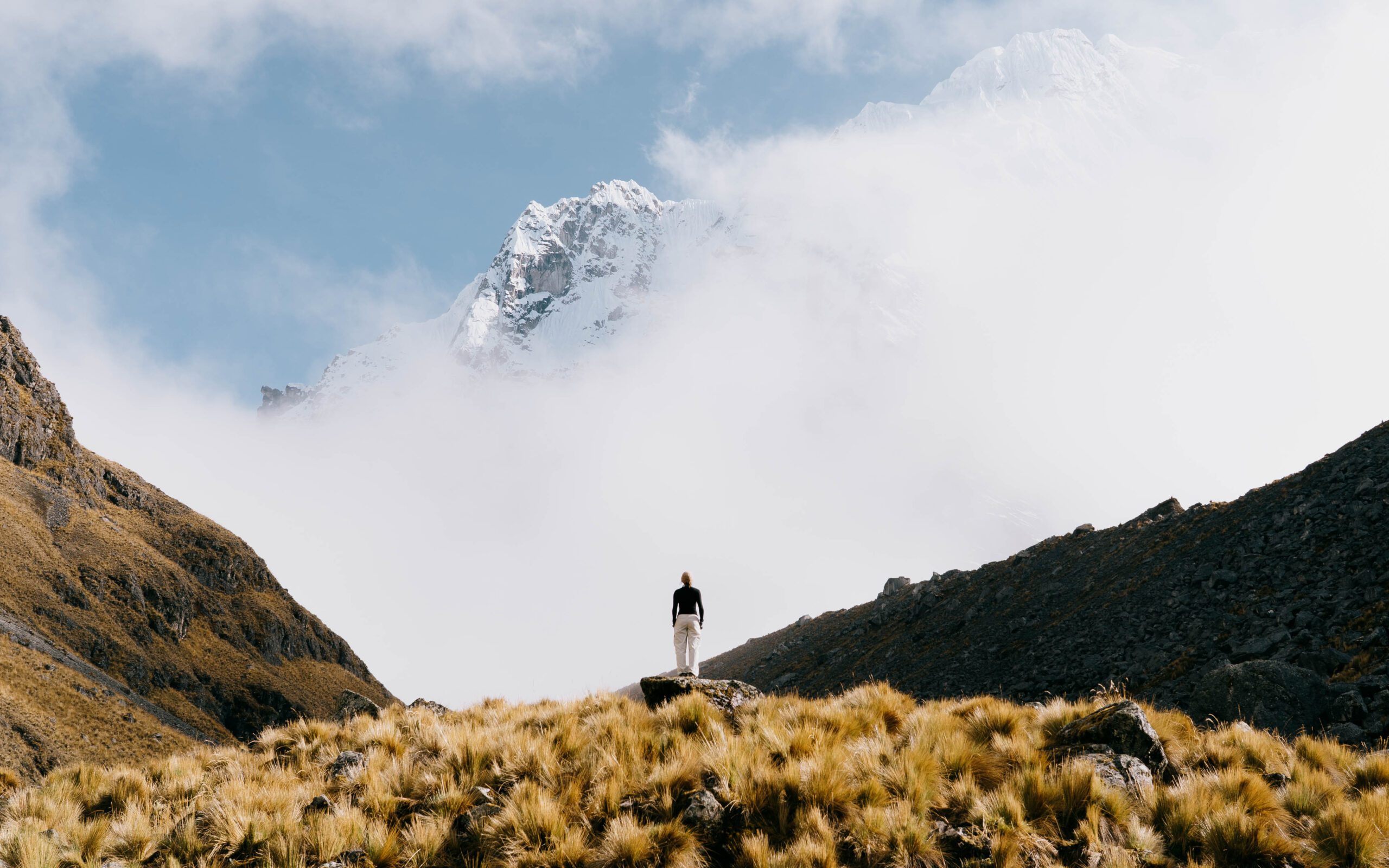 Woman standing on a rock gazing up at the snow-capped peak of Salkantay mountain surrounded by clouds on the Salkantay Trek, Peru