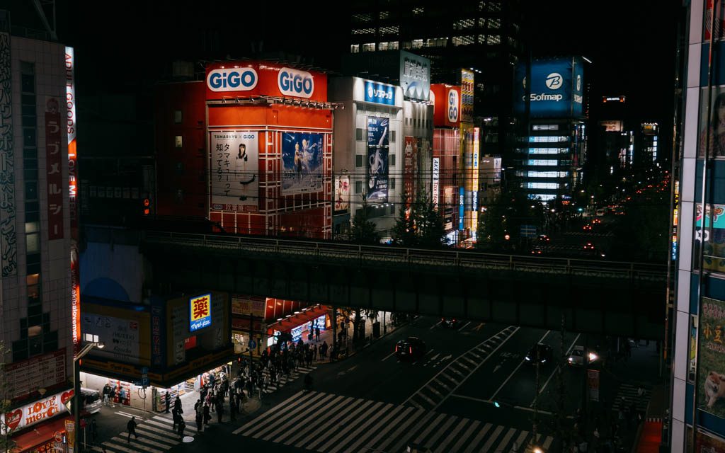Aerial night view of Akihabara's neon-lit arcade buildings and train bridge