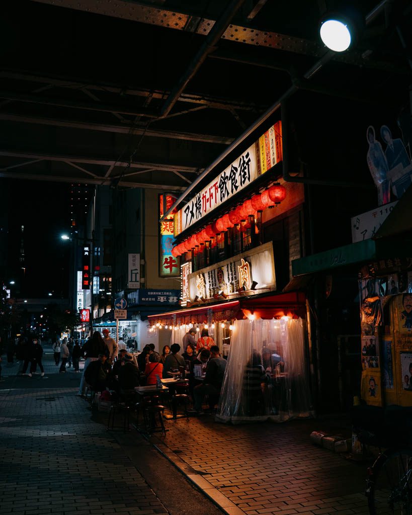 Diners seated at a lantern-lit izakaya stall beneath the train tracks in Ameyoko
