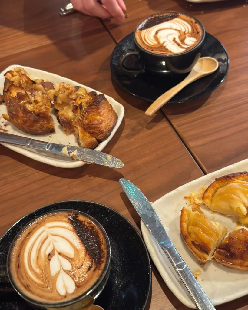 Two lattes with latte art alongside flaky pastries and an apple tart on a wooden table at a café in Nozawa Onsen, Japan