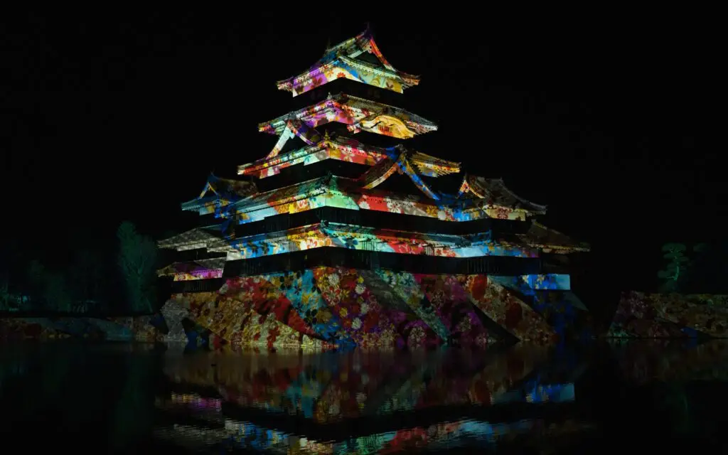 Matsumoto Castle illuminated with vivid colourful floral projections reflected in the surrounding moat at night, Japan
