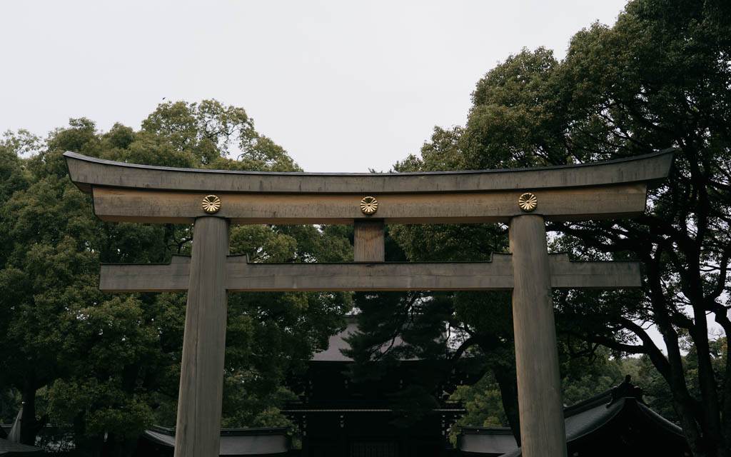 Wooden torii gate with gold imperial crests marking the approach to Meiji Jingu's inner shrine