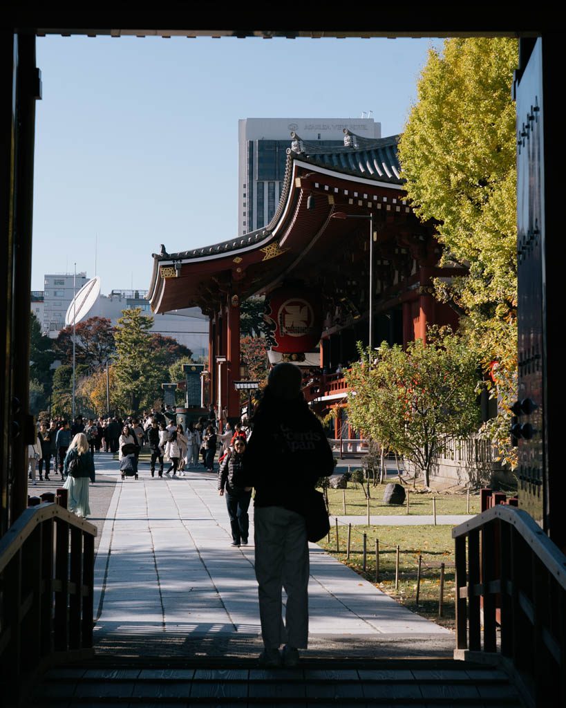 Visitor walking toward Senso-ji temple grounds past autumn trees near Kaminarimon Gate