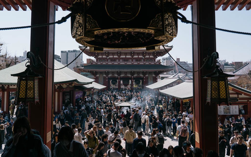 Crowds gathering beneath Hozomon Gate at Senso-ji Temple with incense smoke rising from the censer