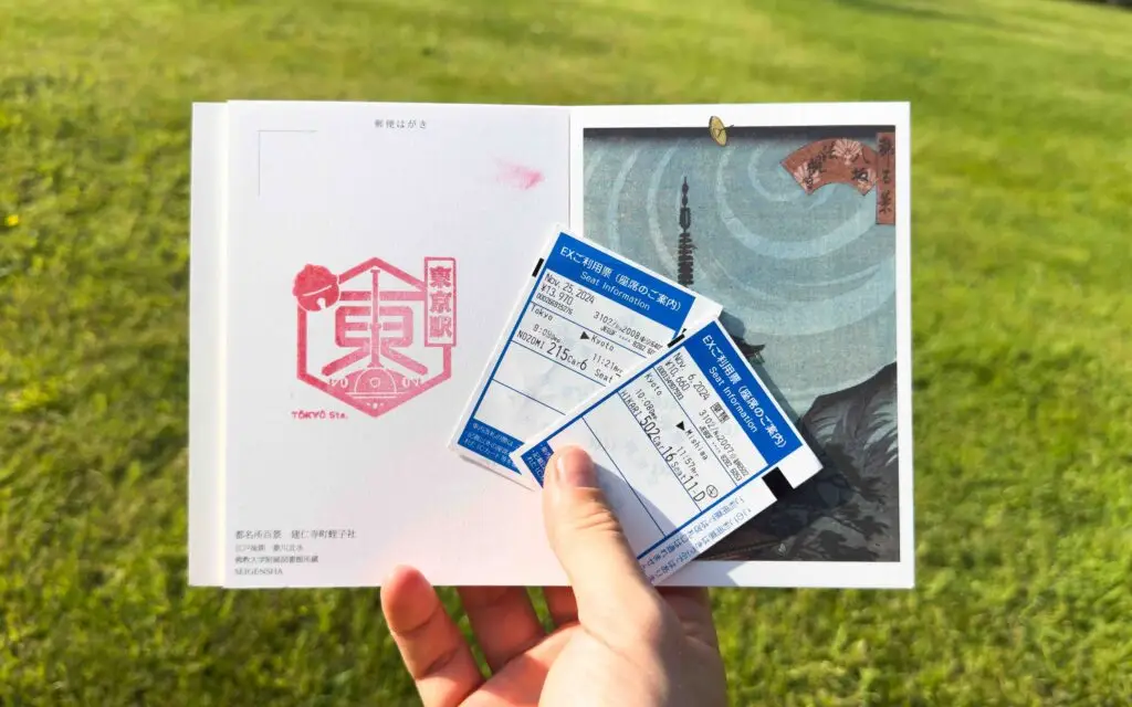 Hand holding two Shinkansen Nozomi seat information tickets printed at the gate alongside a Japanese postcard with a Tokyo Station stamp