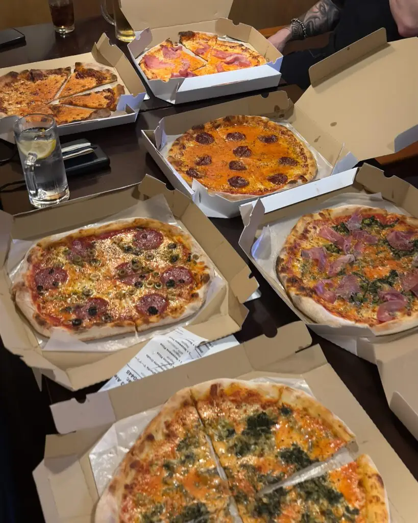 Five pizzas in open boxes spread across a table during a staff night in at the Nozawa Onsen share house, Japan ski season