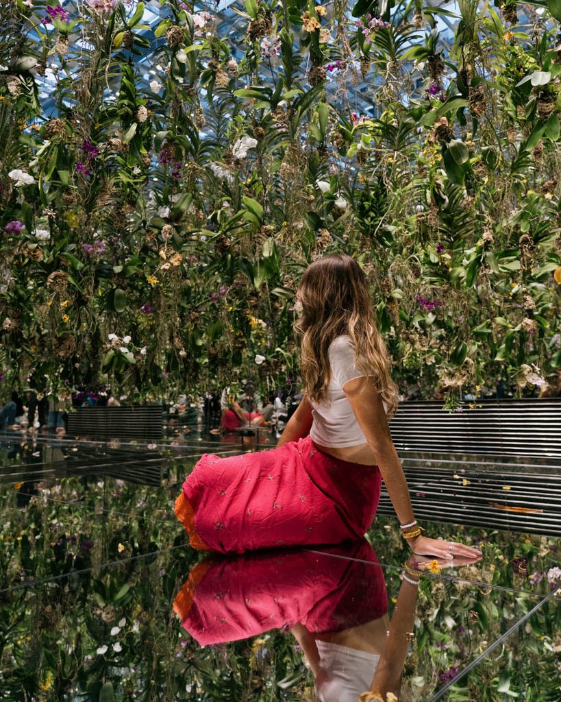 Visitor sitting beneath a suspended garden of orchids reflected in the mirrored floor at TeamLab Planets