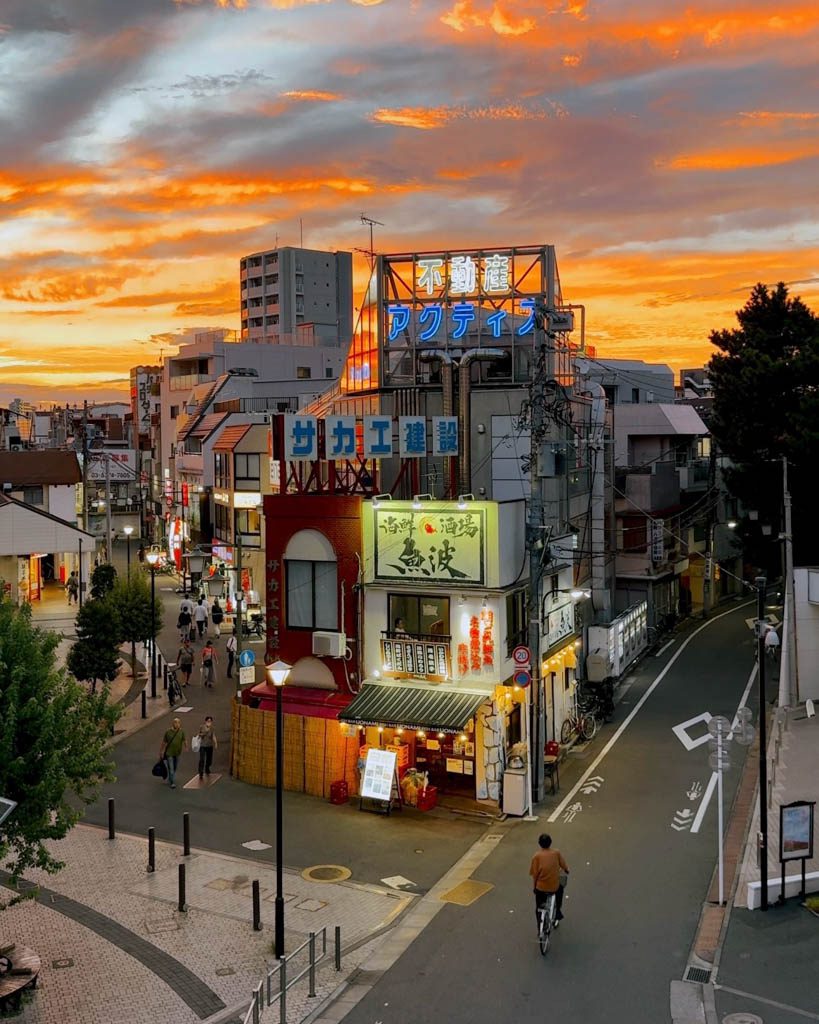 Dramatic orange sunset over a quiet Tokyo neighbourhood street with illuminated shop signage