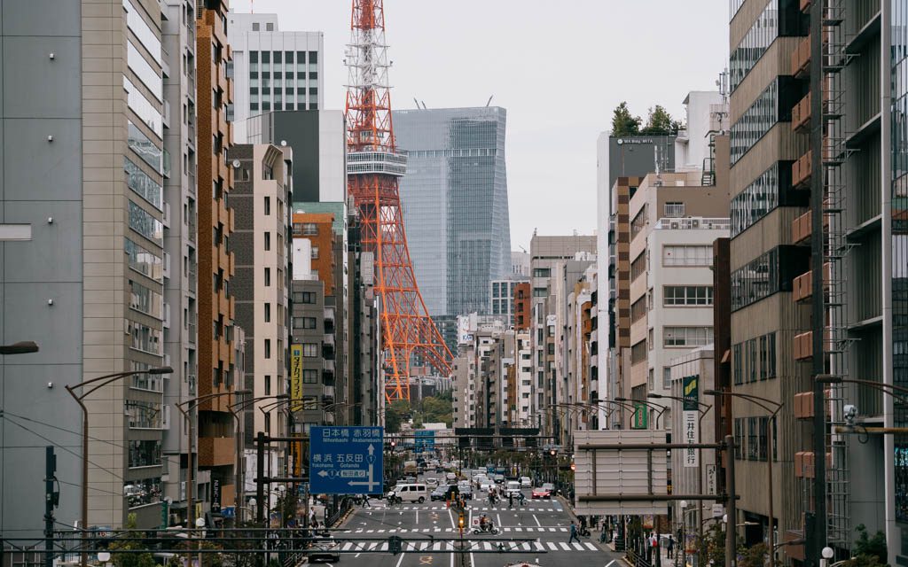 Tokyo Tower rising above a busy Tokyo street with traffic and pedestrians below