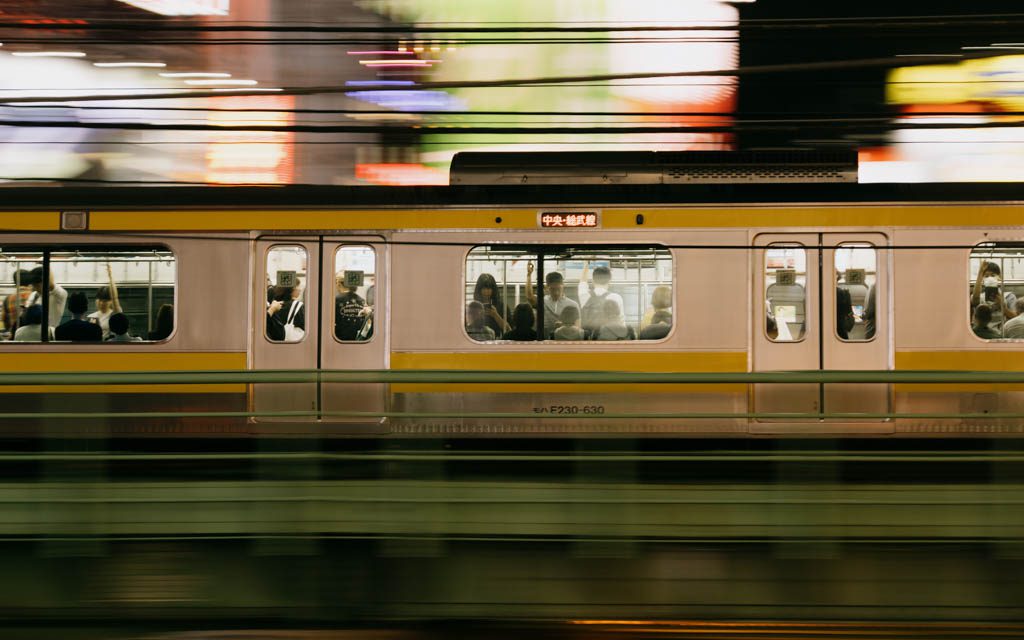 JR train passing at speed with blurred neon lights in the background at night in Tokyo