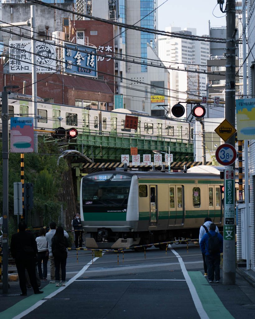 Street-level view of the Yoyogi train crossing with a train passing overhead