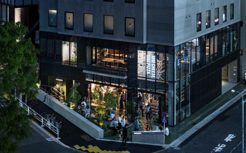 Glass-fronted corner building at night with guests seated in the ground floor cafe area