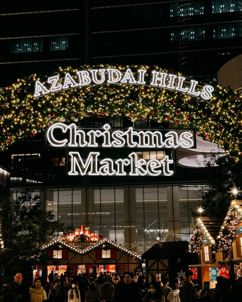 Crowds gathered beneath the illuminated Azabudai Hills Christmas Market entrance sign in Tokyo