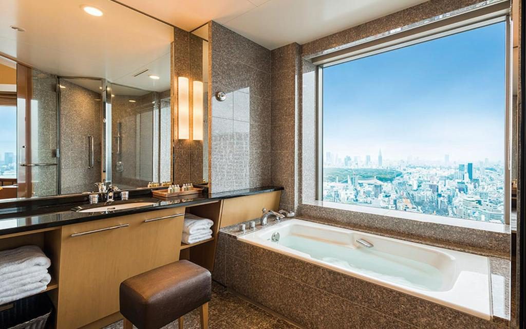 Hotel bathroom with soaking tub beside a floor-to-ceiling window overlooking the Tokyo skyline
