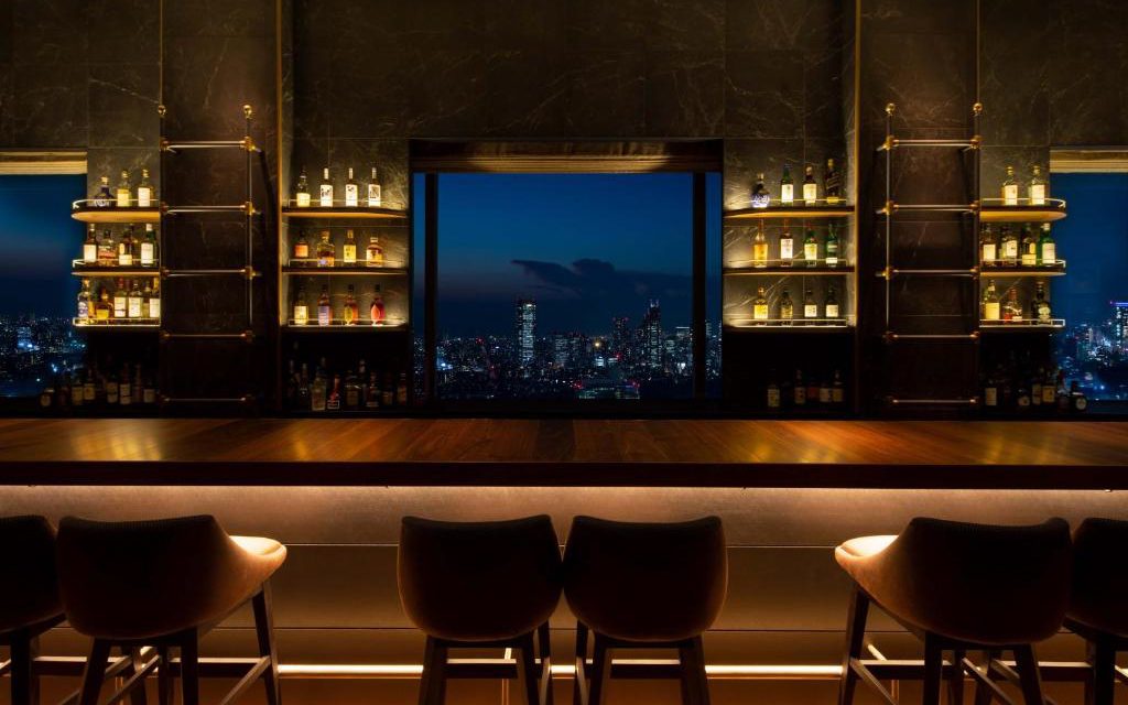 Hotel bar with stocked shelves and bar stools overlooking the Tokyo skyline at night
