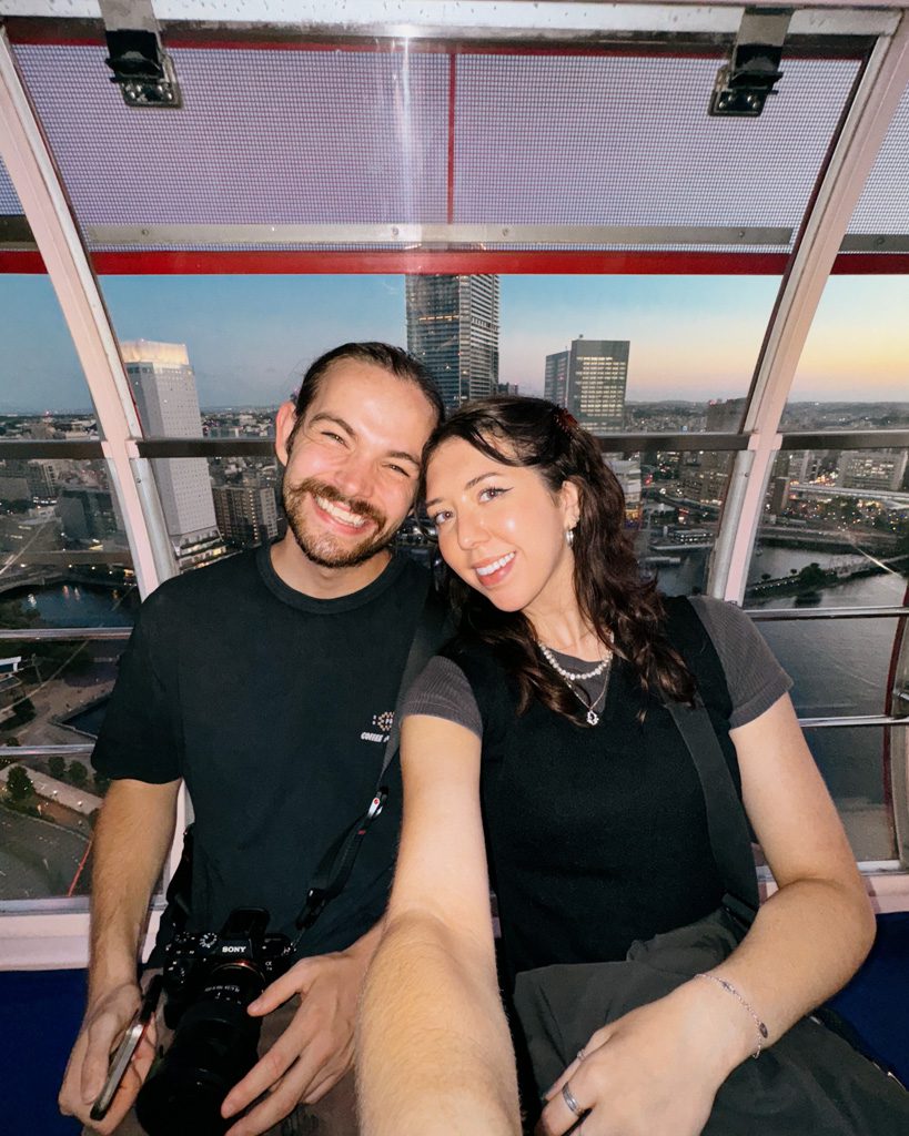 Couple taking a selfie inside a ferris wheel cabin overlooking Yokohama's cityscape at dusk