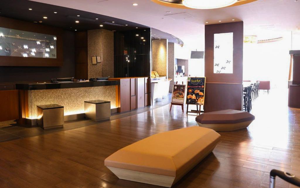 Hotel lobby with wooden reception counter, hanging round pendant light, and modern seating benches