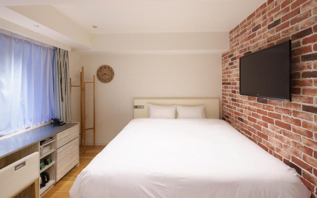 Hotel room with white double bed, exposed brick feature wall, and wall-mounted TV