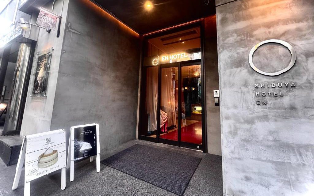 Glass entrance doorway of EN Hotel Shibuya with illuminated signage and concrete facade