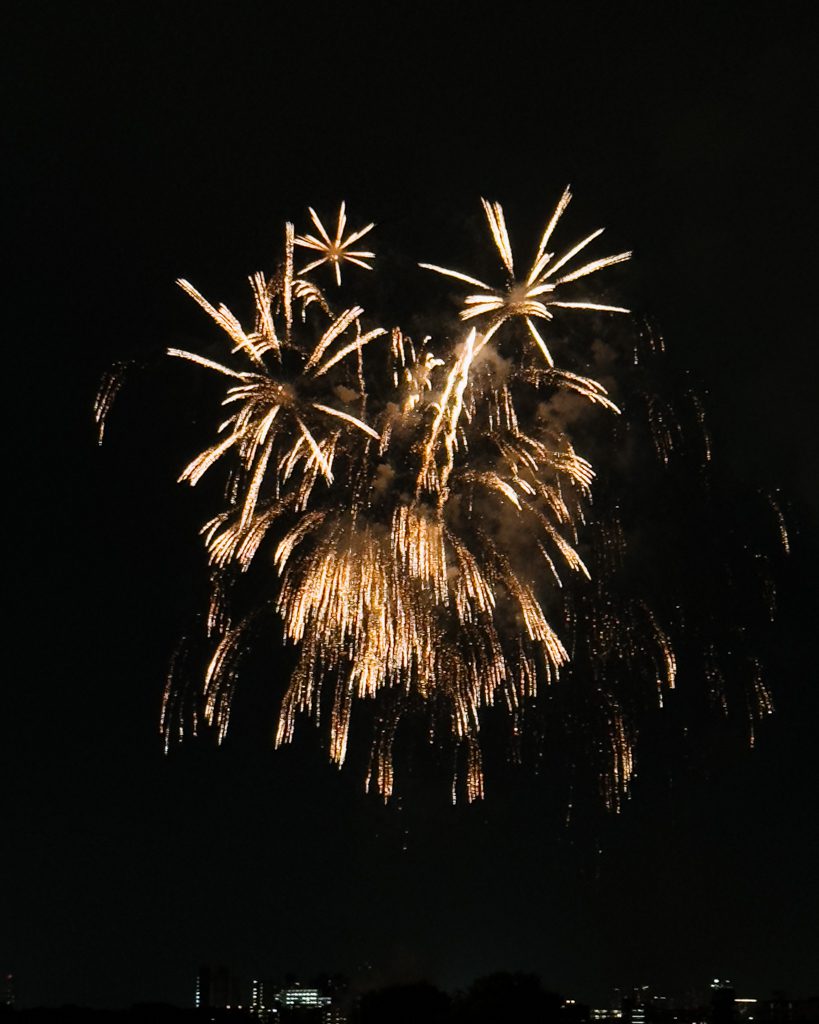 Gold hanabi fireworks bursting over the Tokyo skyline at night during summer festival season