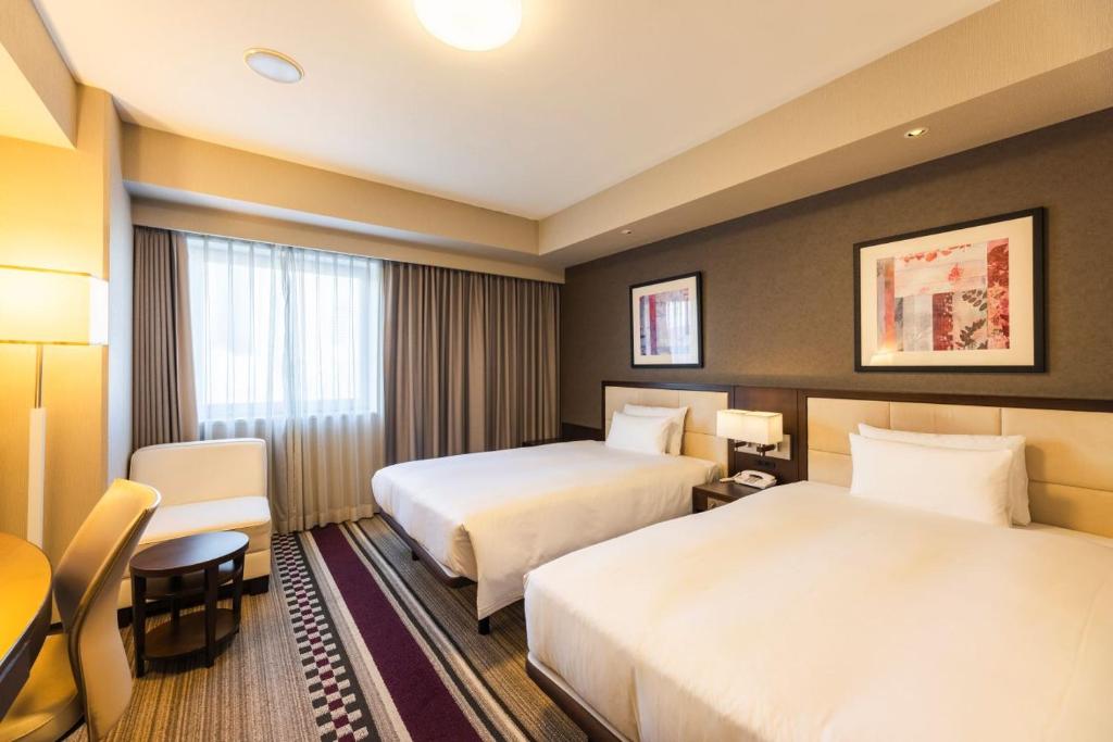 Twin hotel room with two double beds, patterned rug, and city-facing window