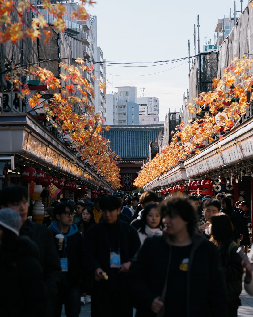 Crowds walking through Nakamise shopping street in Asakusa with orange autumn maple leaves overhead