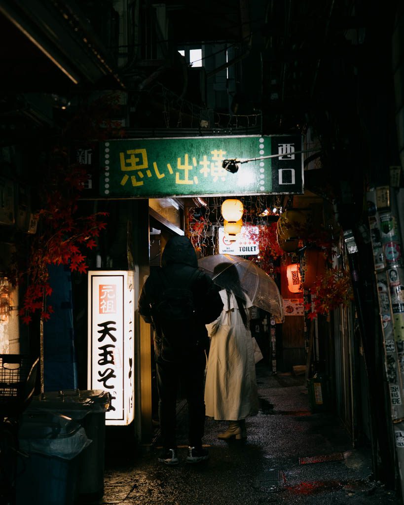 Omoide Yokocho entrance sign in Shinjuku with couple sheltering under umbrella