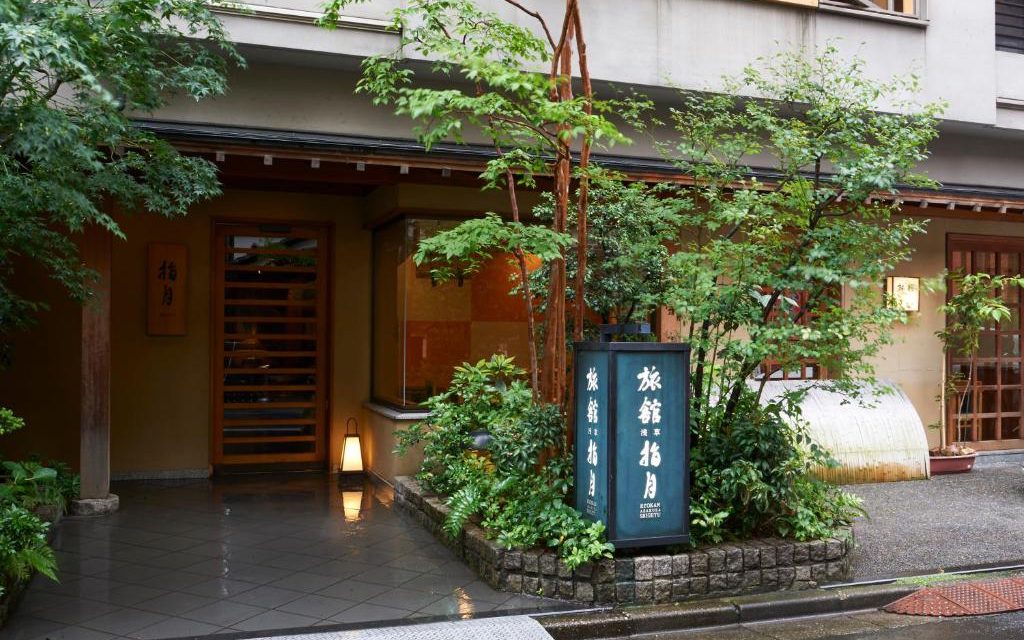 Traditional wooden entrance to Ryokan Asakusa Shigetsu with lantern and greenery on a rainy evening