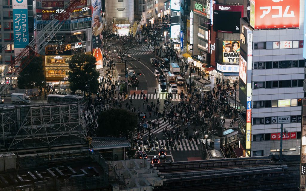 Aerial view of Shibuya Scramble Crossing at dusk with crowds and neon signage