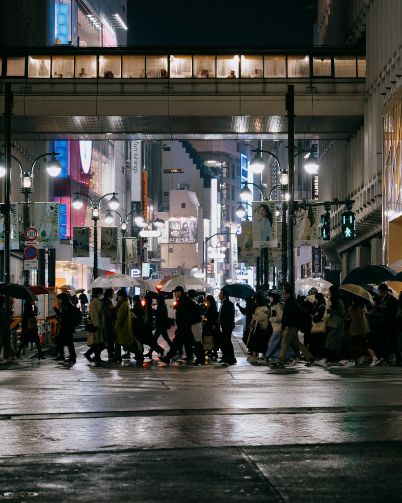 Pedestrians crossing a rainy Shibuya street at night under umbrellas