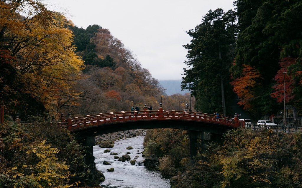 Red arched bridge crossing a river in Nikko surrounded by autumn foliage