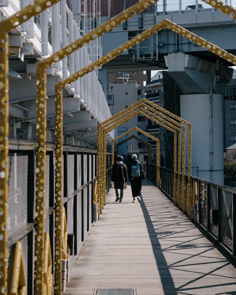 Couple walking through the golden arched walkway on the Sumida River Walk near Asakusa