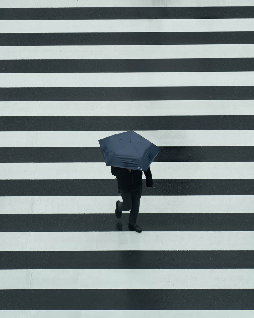 Aerial view of a pedestrian with umbrella crossing a striped Tokyo road