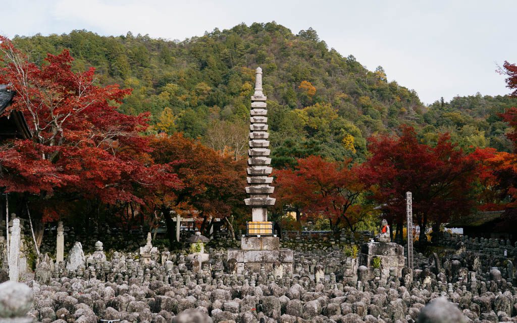 Rows of stone statues with a stone pagoda and autumn trees at Adashino Nenbutsu-ji