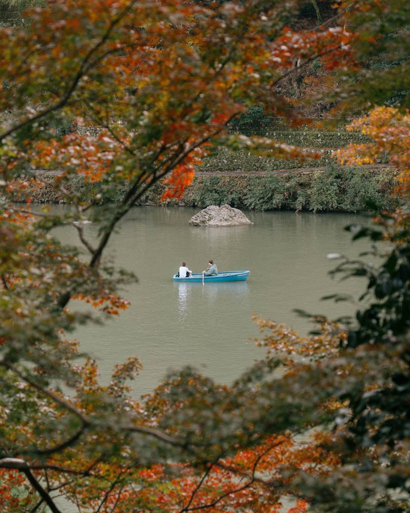 Two people in a rowboat on the river at Arashiyama, framed by autumn leaves