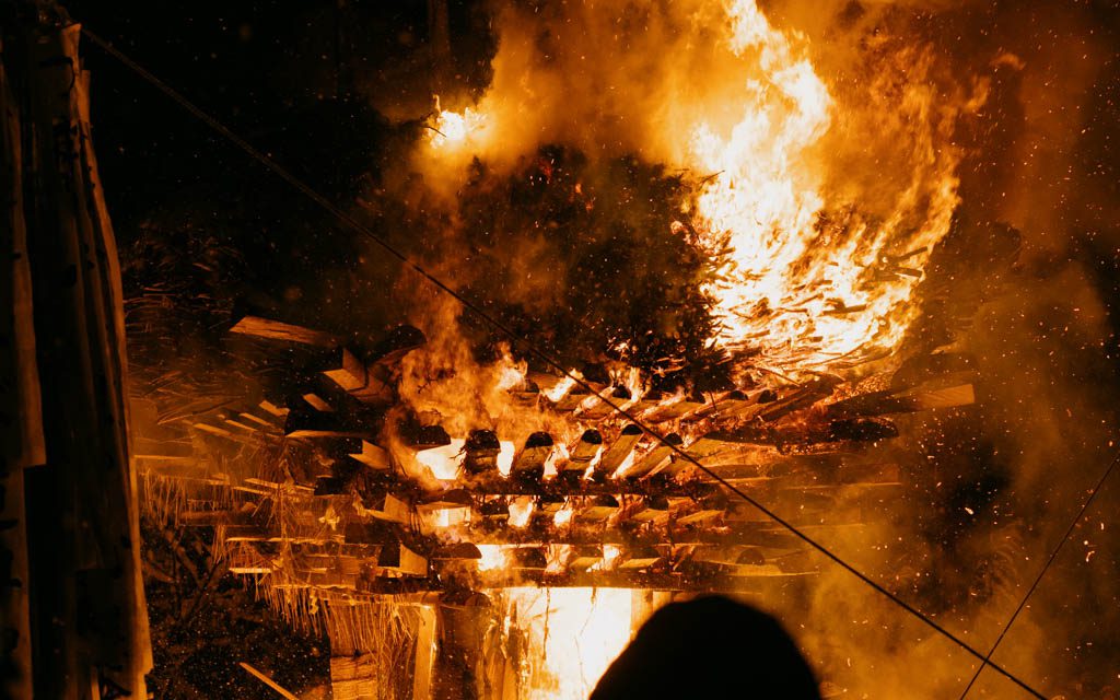 The shaden pyre engulfed in flames at night during the Dosojin Fire Festival, with sparks and smoke rising above the burning timber
