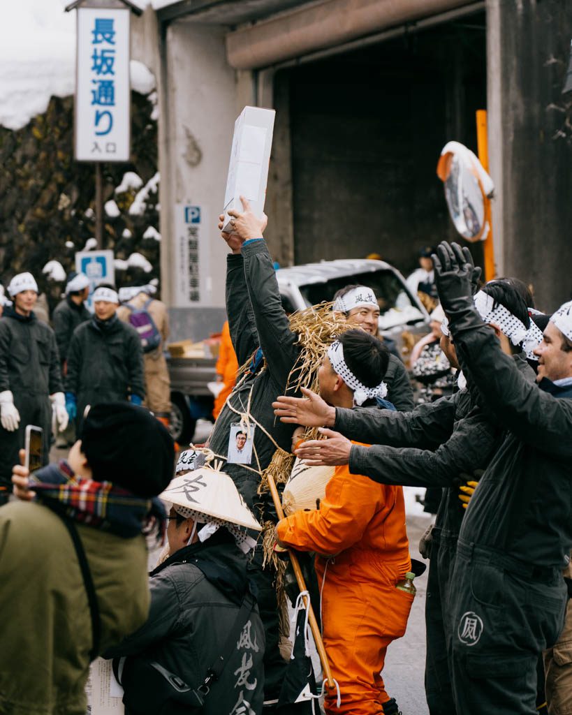 Participants in straw capes and headbands raising their arms as a donation is held aloft during the Dosojin Fire Festival in Nozawa Onsen