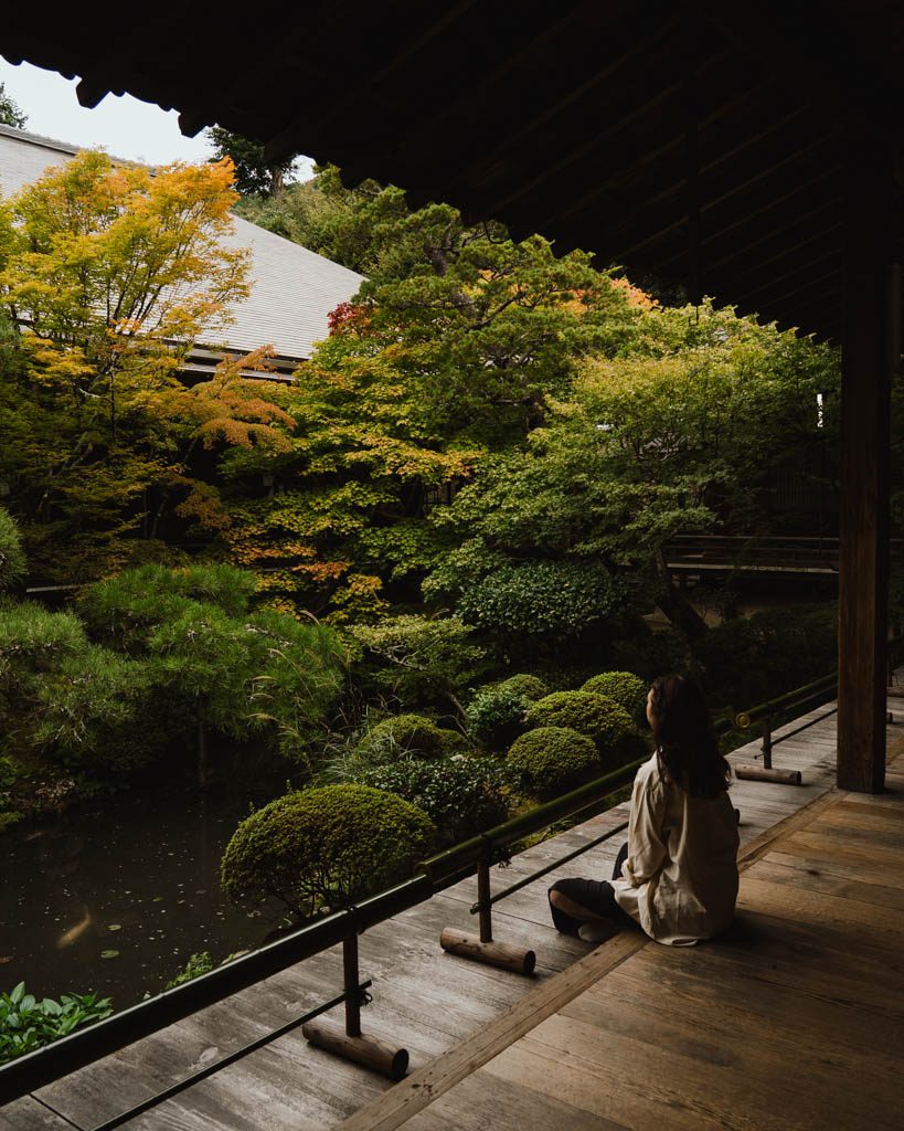 Woman sitting on a wooden veranda overlooking the garden and pond at Eikan-do