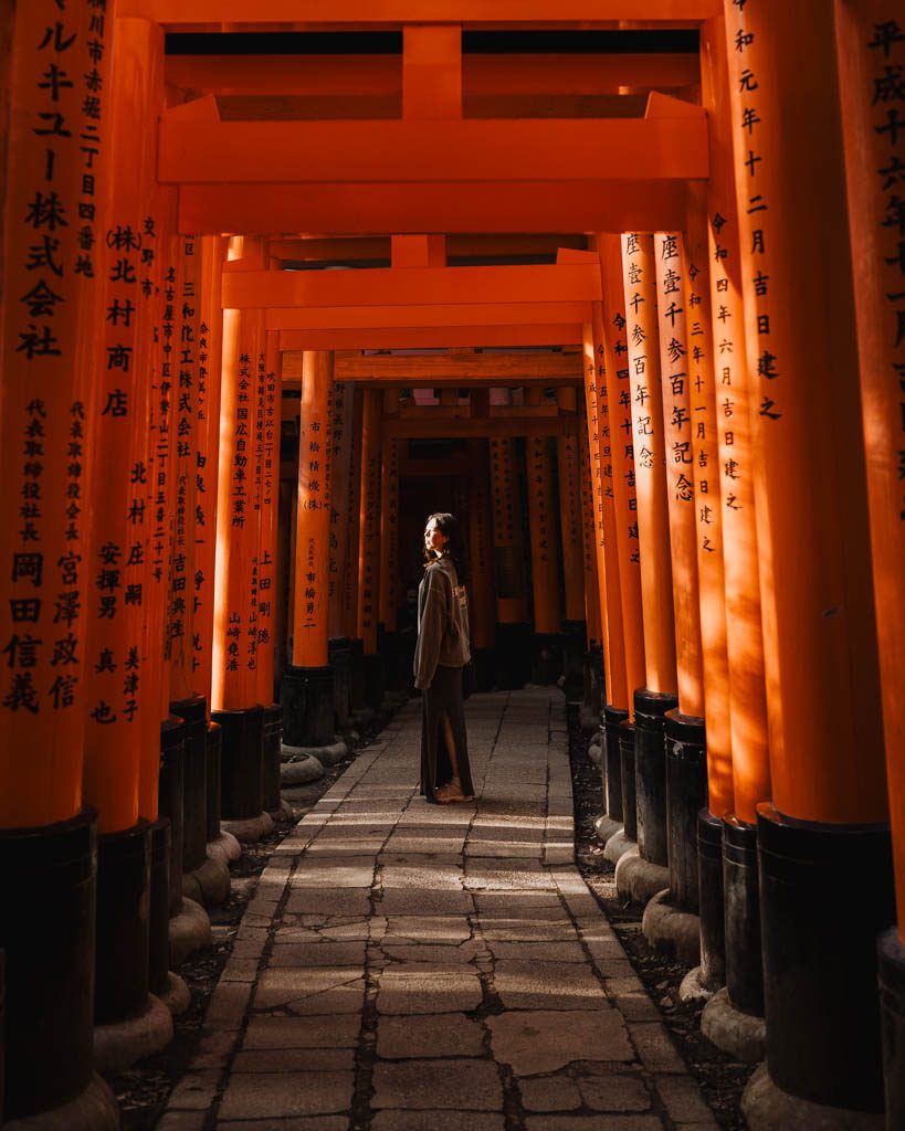 Person standing beneath the tunnel of torii gates at Fushimi Inari Shrine
