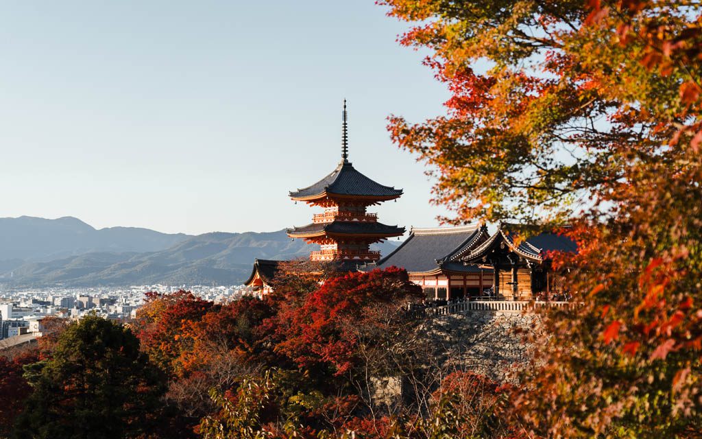 Kiyomizu-dera's pagoda surrounded by autumn foliage with the Kyoto skyline in the background