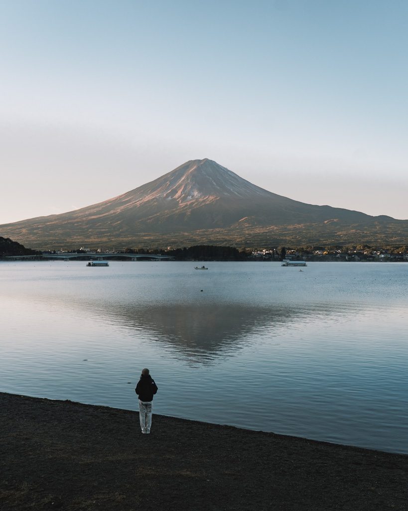Person standing on the shoreline of Lake Kawaguchiko facing Mt Fuji