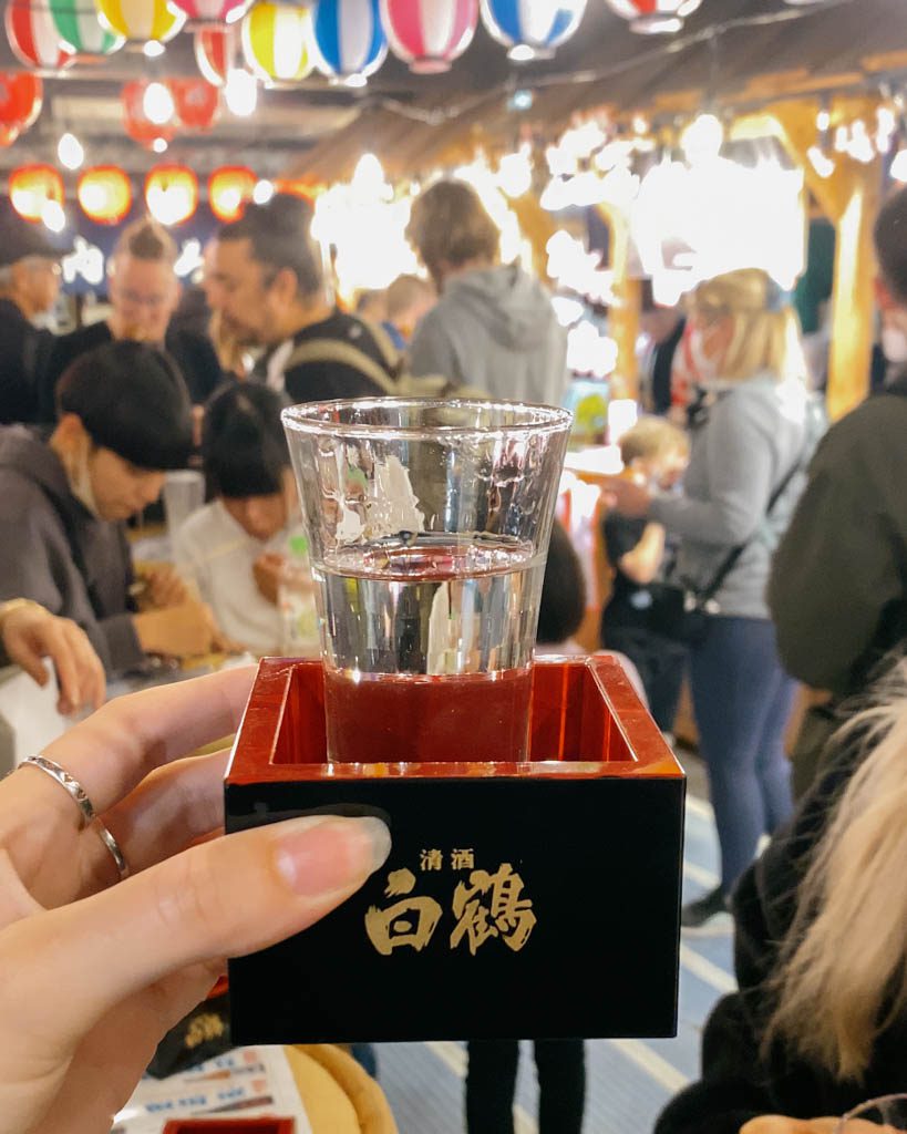 A ¥100 glass of sake served in a traditional masu box at Nishiki Market