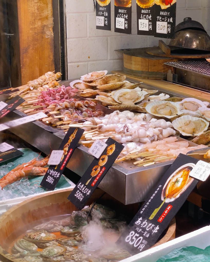 Fresh seafood skewers and shellfish on display at a food stall in Nishiki Market