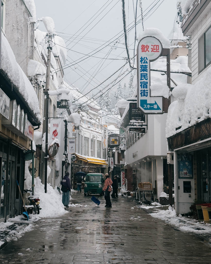 Snowy village alley in Nozawa Onsen lined with shops and minshuku signs