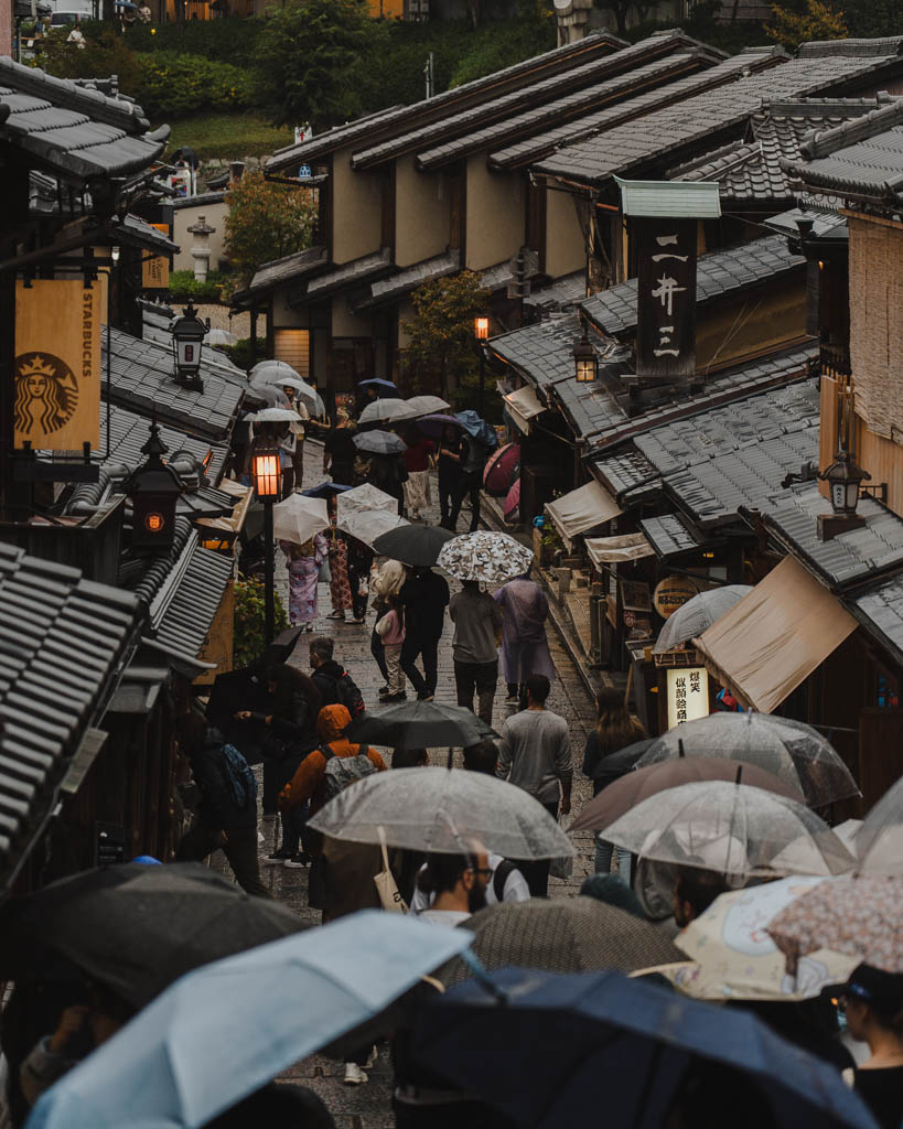 Crowds with umbrellas on a rainy day at Sannenzaka, with a Starbucks sign visible among the traditional buildings